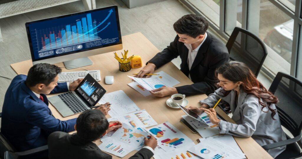 Project team of two men and one woman at desk and viewing multiple devices, analyzing data about on premises vs cloud ERP